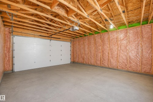 Spacious garage with exposed wood ceiling trusses, concrete flooring, and an insulated garage door - 6453 177A Avenue Nw, Edmonton, AB 