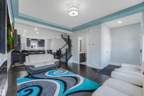 Recessed lighting throughout, dark wood-finish flooring, a white stone-faced fireplace, and a dark wood staircase with white risers - 6453 177A Avenue Nw, Edmonton, AB 