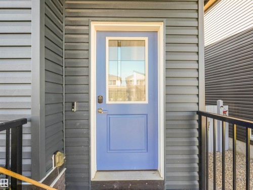 Entry door with upper glass panel, dark gray horizontal siding, and black metal railing - 6453 177A Avenue Nw, Edmonton, AB 