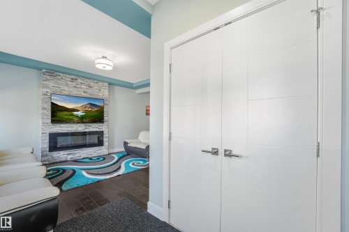 Stacked stone fireplace with an integrated electric insert, wood-finish flooring, and contemporary overhead lighting - 6453 177A Avenue Nw, Edmonton, AB 