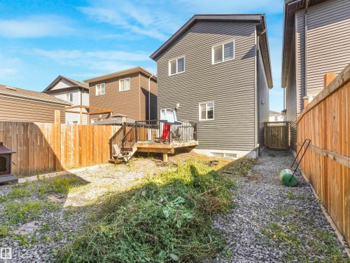 Rear exterior featuring horizontal siding, multiple windows, a wood deck with stairs, a wood fence, and a gravel yard - 6453 177A Avenue Nw, Edmonton, AB 