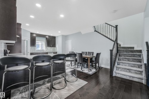 Open-concept living space featuring dark wood-finish flooring, recessed lighting, a kitchen island with seating, dark cabinetry, and a carpeted staircase with dark railings - 6453 177A Avenue Nw, Edmonton, AB 