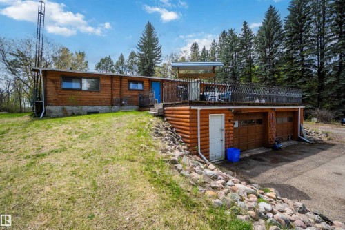 Log-style exterior featuring an upper-level deck, two garage bays, a lower-level access door, and surrounding mature trees - 910 Hermitage Avenue, Rural Parkland County, AB - Outdoor