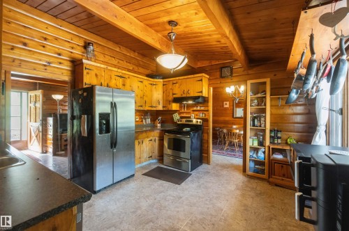 Rustic kitchen featuring wood-paneled walls and ceiling, exposed wood beams, and wood cabinetry with dark hardware - 910 Hermitage Avenue, Rural Parkland County, AB - Indoor Photo Showing Kitchen
