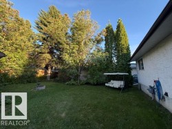 Expansive backyard featuring a manicured lawn, established trees, and a built-in fire pit - 