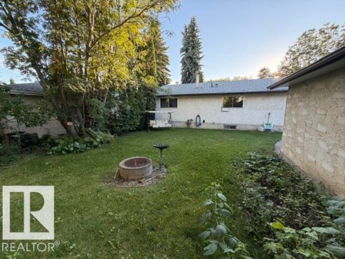 Expansive green lawn with mature trees, stone fire pit, and bird bath - 3 Morgan Crescent, St. Albert, AB 