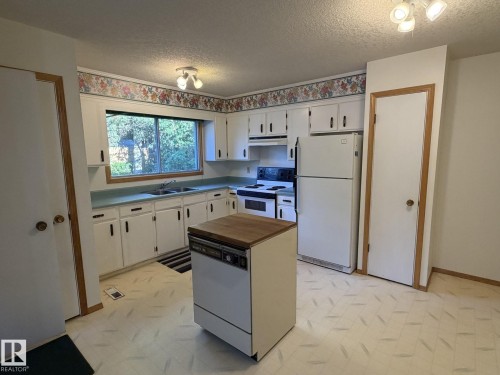 Kitchen featuring white cabinetry, light-toned countertops, a double-basin sink, and a center island with a wood-finish top - 3 Morgan Crescent, St. Albert, AB 