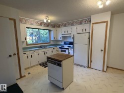 Kitchen featuring white cabinetry, light-toned countertops, a double-basin sink, and a center island with a wood-finish top - 