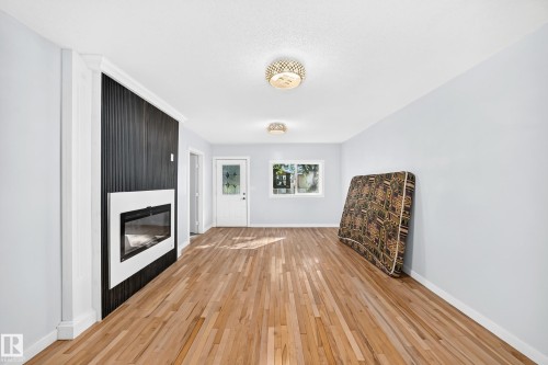 Hardwood flooring, recessed fireplace with white surround, dark wood-finish accent wall, white door with decorative glass inserts, and flush-mount ceiling lighting - Edmonton, AB 