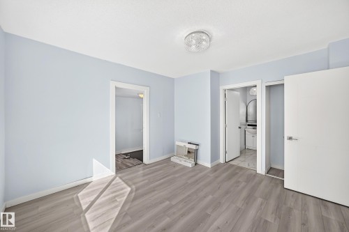 Wood-finish flooring, light blue wall paint, modern crystal flush mount light, white interior doors, and a bathroom vanity with an arched mirror - Edmonton, AB 