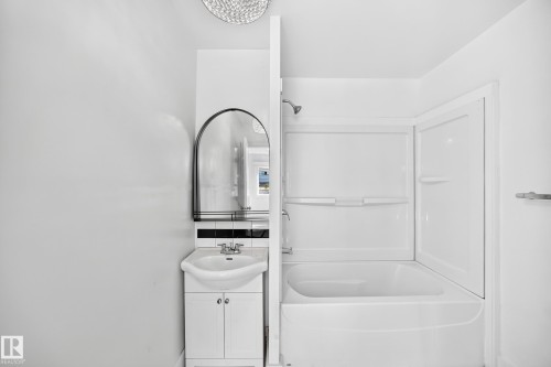 White vanity with a ceramic basin, arched mirror, tiled backsplash, and built-in tub with a shower fixture - Edmonton, AB 