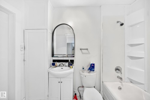 Bathroom featuring a vanity with an integrated sink, a rounded arch mirror, a built-in shower/tub combination with shelving, and a toilet - Edmonton, AB 