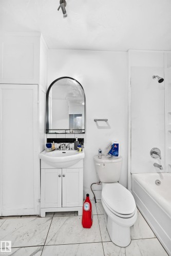 White-tiled flooring, white vanity with cabinet storage, arched vanity mirror, and white bathtub with shower - Edmonton, AB 