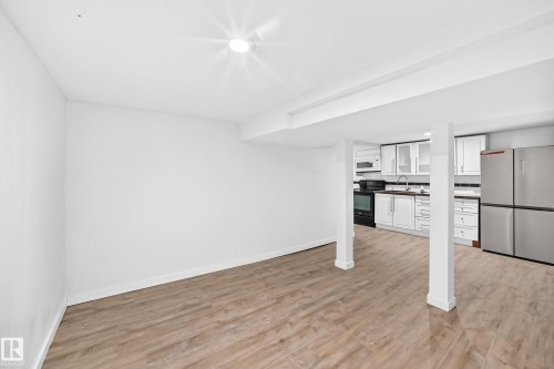 Open-concept area featuring wood-finish flooring, recessed lighting, and a kitchen with white cabinetry, stainless steel appliances, and a tile backsplash - Edmonton, AB 