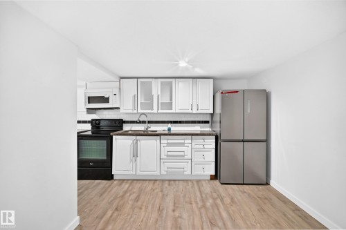 Kitchen featuring white cabinetry, wood-finish flooring, a stainless steel refrigerator, a black electric range, and a white microwave - Edmonton, AB 