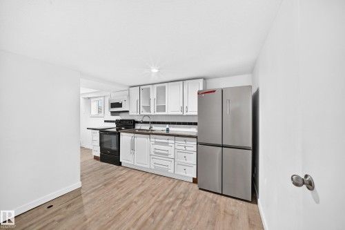 Kitchen featuring wood-finish flooring, white cabinetry, dark countertops, and stainless steel appliances - Edmonton, AB 