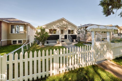 White picket fence with an arched entry, manicured front lawn, and mature landscaping - Edmonton, AB 