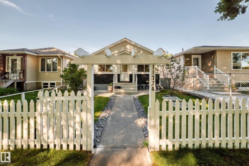 Picket fence entry with an integrated arbor, leading to a concrete pathway flanked by decorative rock beds and manicured lawn - Edmonton, AB 