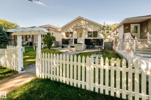 White picket fence, arched entryway with house numbers, concrete walkway, and a manicured lawn - Edmonton, AB 
