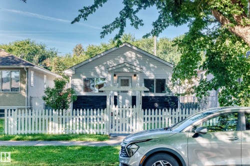Light-colored siding exterior, gabled roofline, front porch with decorative columns, white picket fence, and established landscaping - Edmonton, AB 