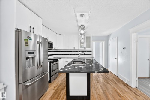 White cabinetry with black hardware, stainless steel appliances, dark island with integrated sink, wood-finish flooring, and pendant lighting - Edmonton, AB 