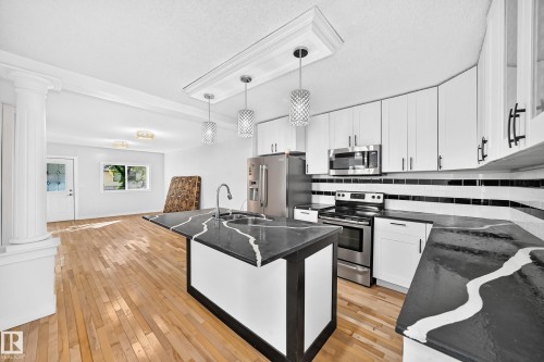 Kitchen featuring white cabinetry, stainless steel appliances, black and white countertops, and pendant lighting - Edmonton, AB 