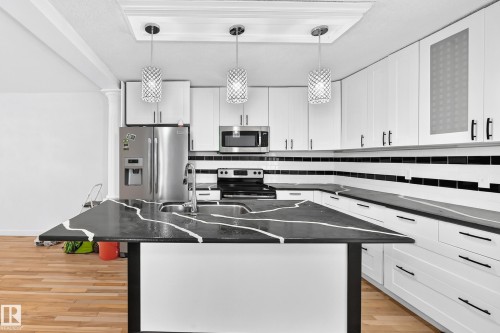 White cabinetry with black hardware, black and white tile backsplash, stainless steel appliances, black and white patterned countertops, and wood-finish flooring - Edmonton, AB 