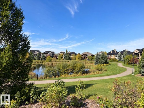 Lush green landscaping with a winding pathway, a serene pond with natural vegetation, and a backdrop of residential properties - 885 Windermere Wynd Nw, Edmonton, AB 