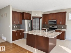Kitchen featuring a central island with a stone-finish countertop, wood-finish cabinetry, stainless steel appliances, and a pantry with built-in shelving - 