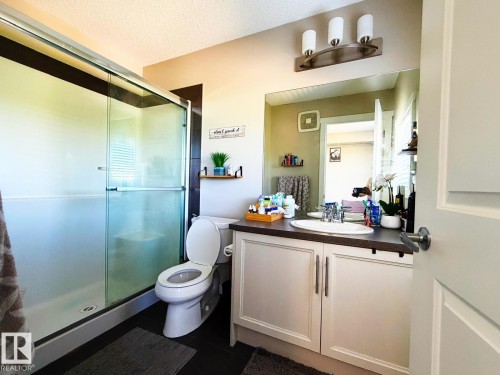 Glass-enclosed shower with a white base, single vanity with a white basin sink, dark countertop, and light-toned cabinetry - 5169 Chappelle Rd Southwest, Edmonton, AB 