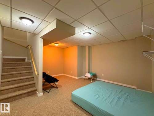 Carpeted stairs with a natural wood handrail, ceiling-mounted light fixtures, and a dropped ceiling - 5169 Chappelle Rd Southwest, Edmonton, AB 