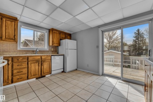 Kitchen featuring wood cabinetry, tiled flooring, and a sliding glass door to an outdoor deck - 3227 145 Avenue Nw, Edmonton, AB 