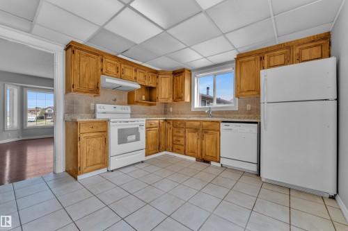 Kitchen featuring wood cabinetry, white appliances, tile flooring, and a window - 3227 145 Avenue Nw, Edmonton, AB 