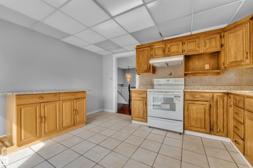 Kitchen featuring extensive wood cabinetry, tile flooring, and a white electric range - 3227 145 Avenue Nw, Edmonton, AB 