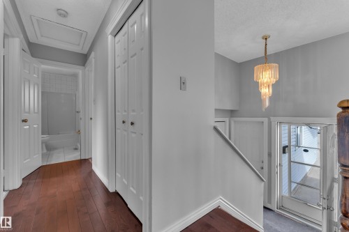Hardwood-finish flooring, white paneled doors, built-in bi-fold closet, contemporary chandelier, and a white tiled bathroom - 3227 145 Avenue Nw, Edmonton, AB 