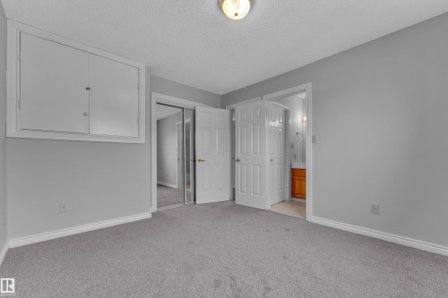Carpeted room featuring a ceiling-mounted light fixture, white trim, sliding mirrored closet doors, and an additional room entry - 3227 145 Avenue Nw, Edmonton, AB 