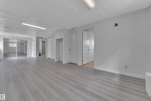Spacious room with light wood-finish flooring, white walls, and a drop ceiling with fluorescent lighting - 3227 145 Avenue Nw, Edmonton, AB 
