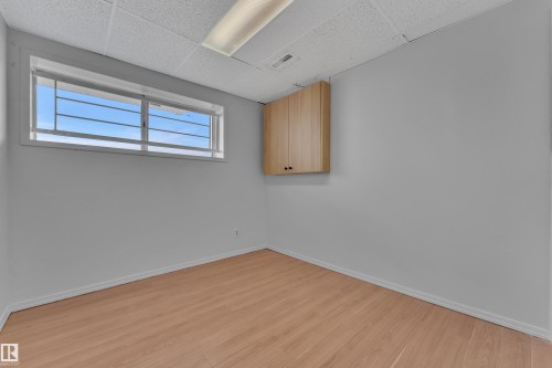 Recessed window with security bars, light wood-finish flooring, drop ceiling with recessed lighting, and wall-mounted cabinetry - 3227 145 Avenue Nw, Edmonton, AB 