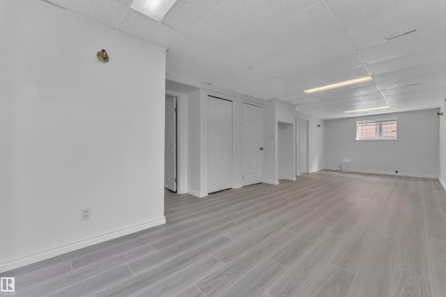 Spacious room featuring wood-finish flooring, white walls, multiple doorways, and a window for natural light - 3227 145 Avenue Nw, Edmonton, AB 