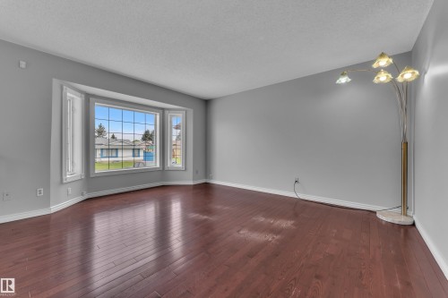 Spacious room featuring a prominent bay window, wood-finish flooring, and light gray wall tones - 3227 145 Avenue Nw, Edmonton, AB 