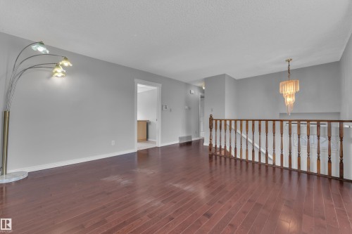 Hardwood flooring, painted walls, open railing, and a tiered chandelier - 3227 145 Avenue Nw, Edmonton, AB 