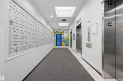 Modern building corridor featuring wall-mounted mailboxes with individual compartments, polished stainless steel elevator doors, recessed ceiling lighting, neutral wall finishes, and gray tile flooring throughout - 