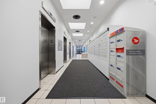 Lobby with multiple stainless steel elevators, recessed lighting, and a mailroom area featuring individual mailboxes and parcel lockers - #1313 10024 Jasper Av Nw, Edmonton, AB 