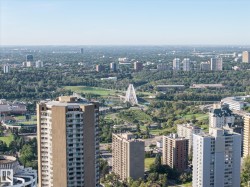 Expansive urban landscape featuring multiple high-rise buildings, extensive green spaces, and a distinctive white arch bridge - 
