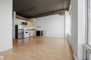 Open-concept living area with wood-finish flooring, exposed concrete ceiling, and track lighting - #1313 10024 Jasper Av Nw, Edmonton, AB 
