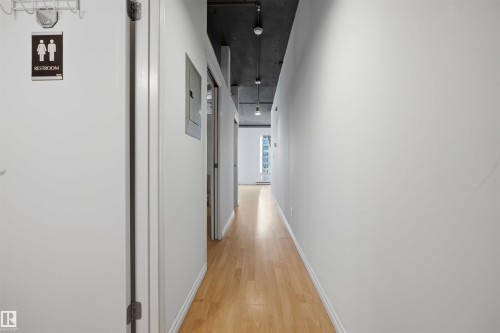 Hallway featuring wood-finish flooring, white walls, exposed ceiling, and track lighting - #1313 10024 Jasper Av Nw, Edmonton, AB 