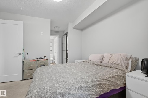 Neutral wall paint, light-toned carpet flooring, and a modern white door with a metal handle - #107 1031 173 St Sw, Edmonton, AB 