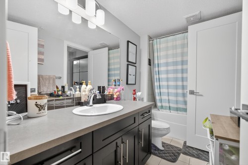 Contemporary vanity with dark wood-finish cabinetry, integrated rectangular sink, and a large wall-mounted mirror - #107 1031 173 St Sw, Edmonton, AB 