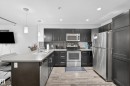 Contemporary kitchen featuring dark cabinetry, stainless steel appliances, light-toned countertops, and wood-finish flooring - #107 1031 173 St Sw, Edmonton, AB 
