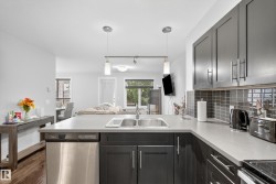 Kitchen featuring dark cabinetry, stainless steel dishwasher, double basin sink, light-toned countertops, and a tiled backsplash - 